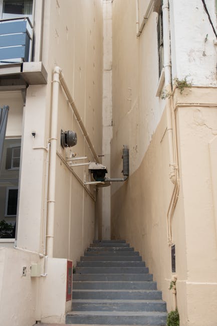 An outdoor stairway leading from a covered walkway with vibrant graffiti on the side walls, featuring concrete steps with rainbow-colored tread strips at the top. The stairs include a metal ramp for a